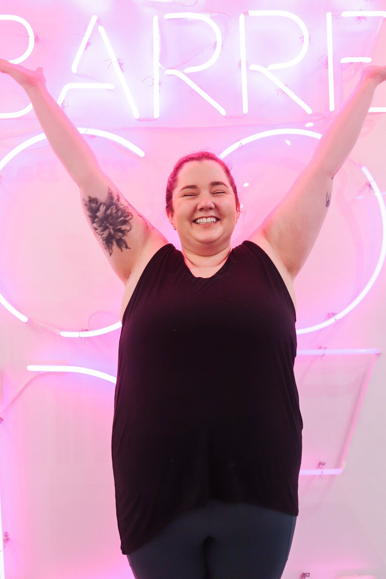 Happy woman in front of the pink neon Barre Code sign in the popular fitness studio in chicago